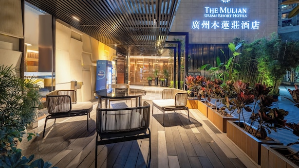 Exterior del Hotel Muilian Urban Resort, con un diseño moderno, que incluye un área de estar al aire libre cubierta con sillas y una mesa, rodeada de plantas en macetas y una entrada bien iluminada.