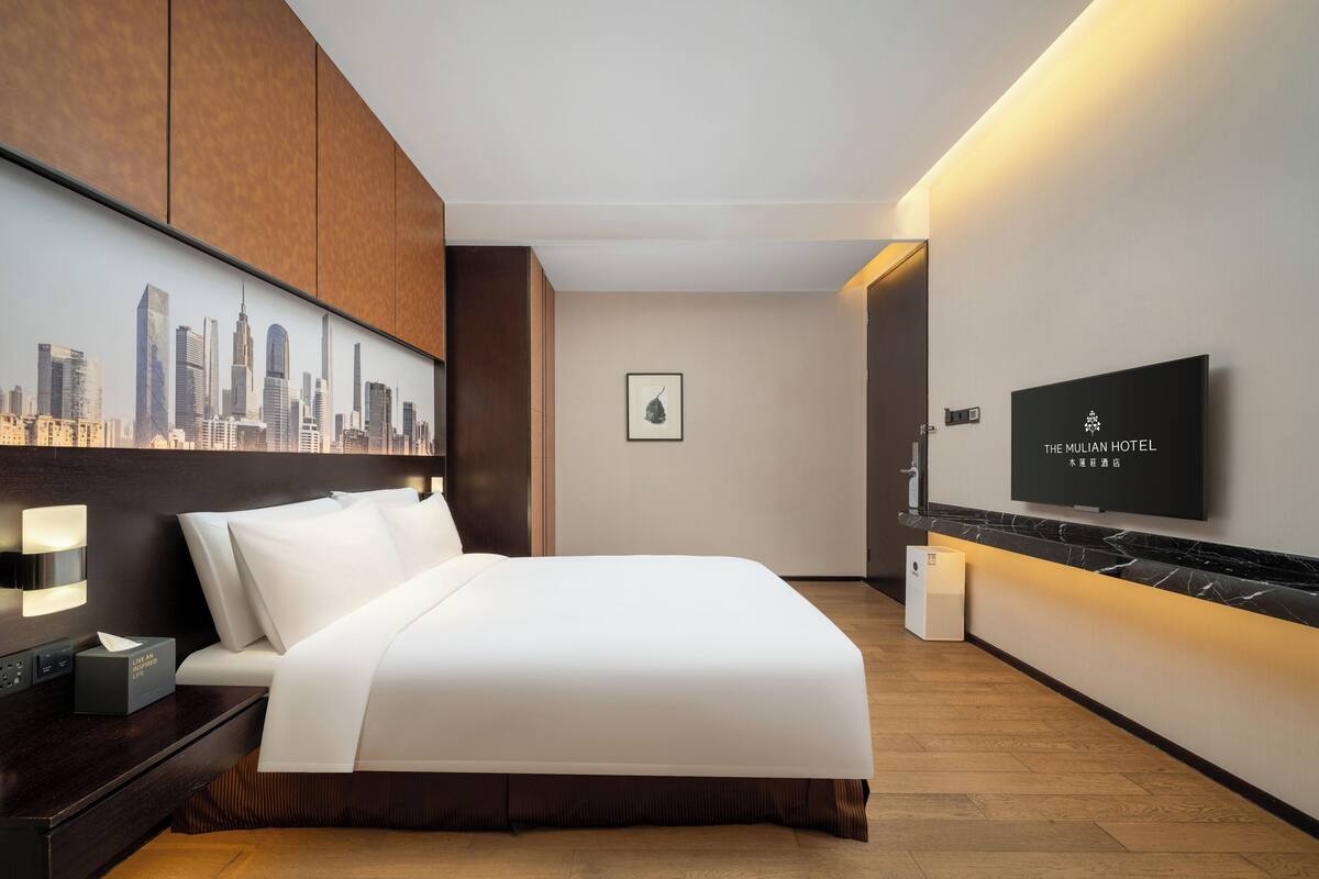 Una camera d'albergo moderna con un grande letto, un'opera d'arte con una veduta sulla città, una TV a schermo piatto e un pavimento in legno.
