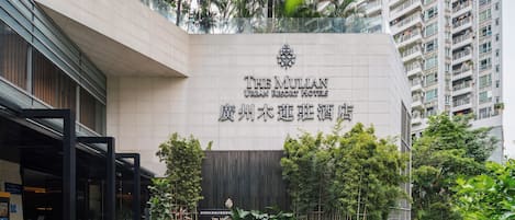 A hotel entrance with a modern facade, a signboard with hotel name, and a landscaped garden area.