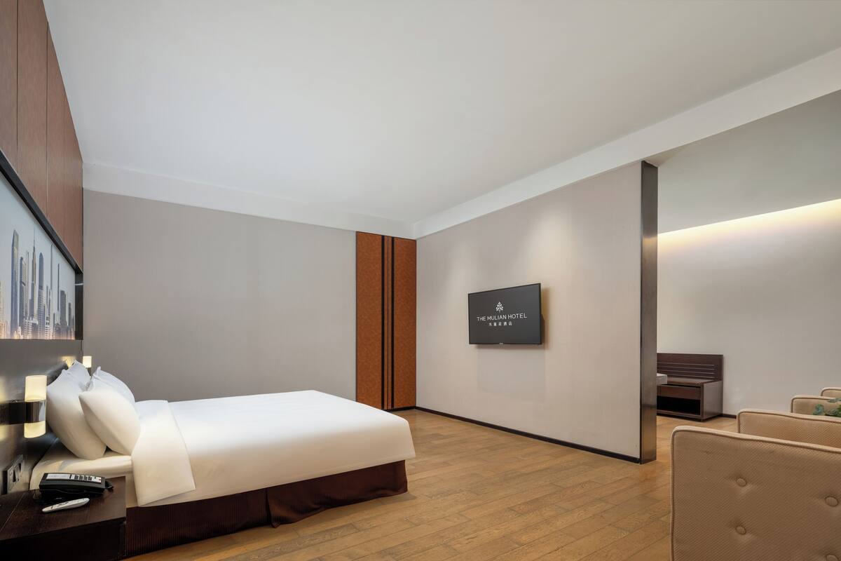 Una camera d'albergo con un letto, un comodino, una lampada e una TV a parete.