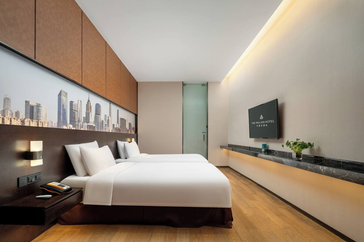 Una camera d'albergo moderna con un grande letto, un murale che raffigura un panorama cittadino, una TV a schermo piatto e un comodino in legno.