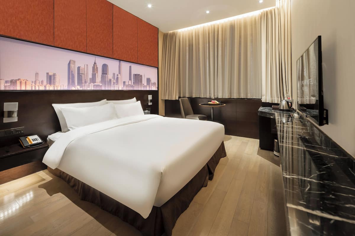Camera d'albergo con un letto grande, vista sulla città, televisore a schermo piatto, un tavolino con un bollitore e un comodino con un telefono.