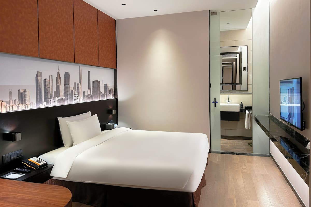 Una camera d'hotel moderna con un letto grande, vista sulla città, bagno con specchio e lavandino e televisione.