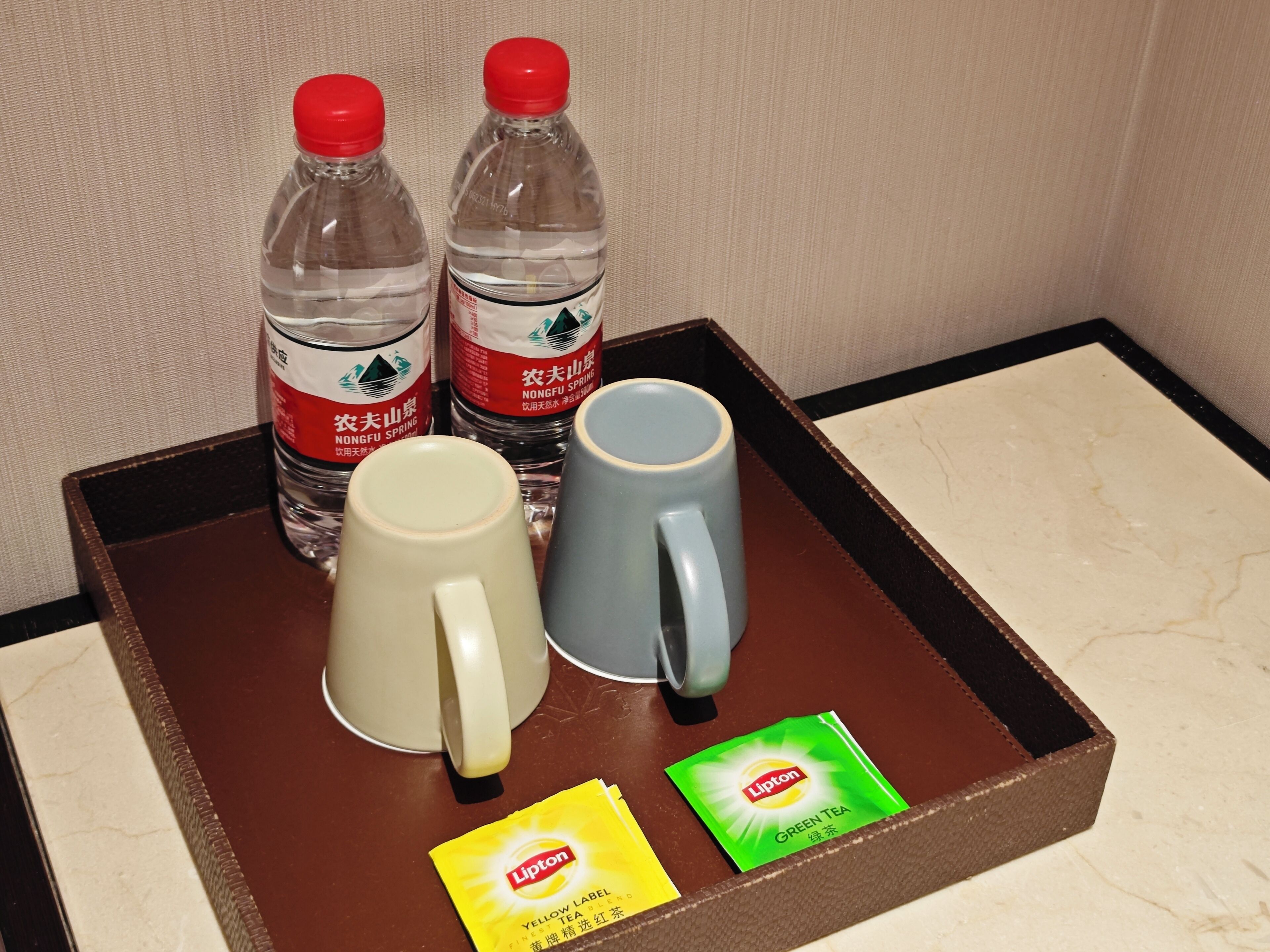 A tray with two water bottles, a beige mug, a blue mug, and two Lipton tea packets.