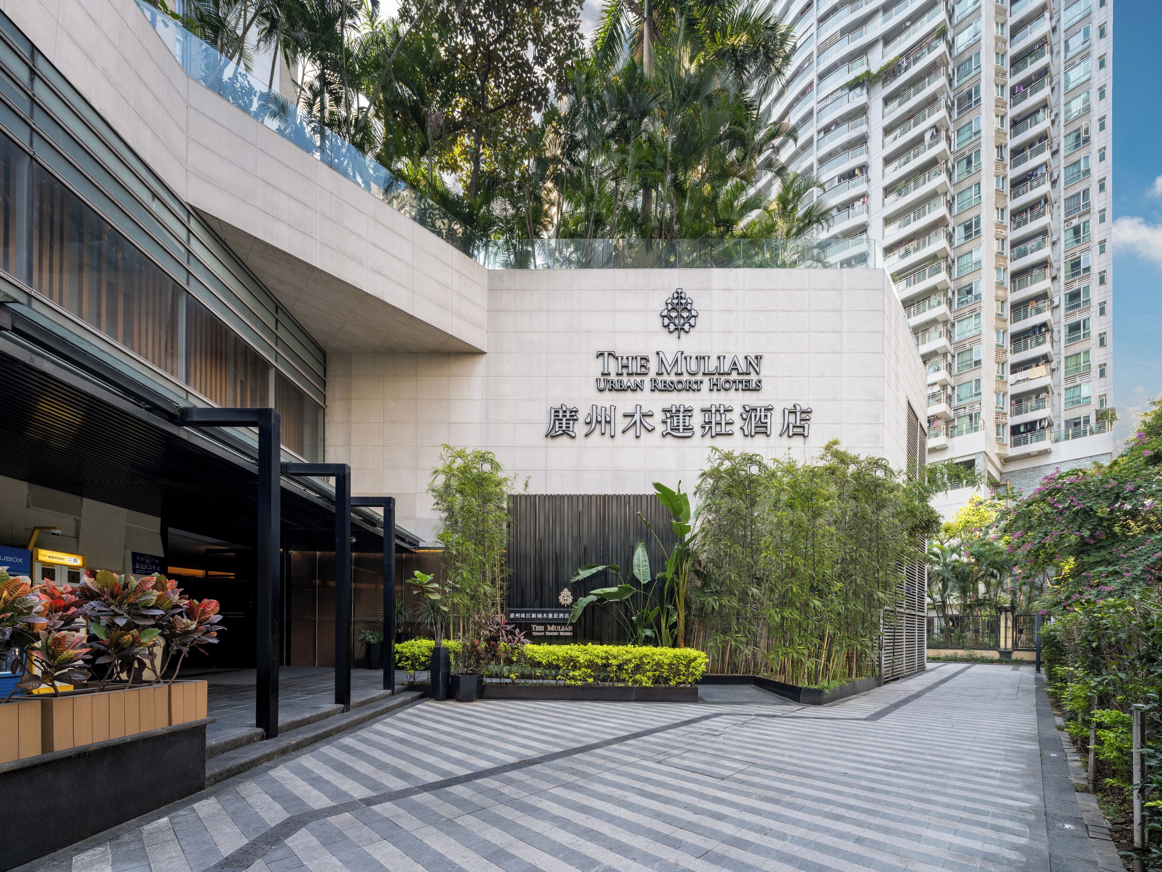 The Mulian Urban Resort Hotel entrance with a modern design, featuring a large signboard, a covered walkway, and surrounding greenery.