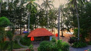 A small building with a red roof surrounded by lush greenery and tall palm trees. - Nataya Roundhouse Coral Bay Resort and Spa (Kampot)