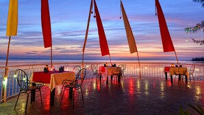 A terrace with tables and chairs, overlooking a body of water at sunset. - Nataya Roundhouse Coral Bay Resort and Spa (Kampot)
