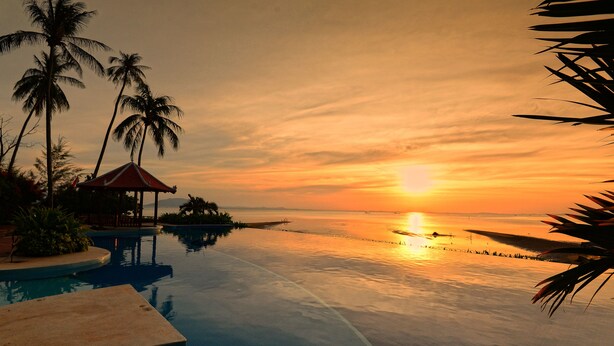 A poolside view with a sunset, palm trees, and a small pavilion. - Nataya Roundhouse Coral Bay Resort and Spa (Kampot)