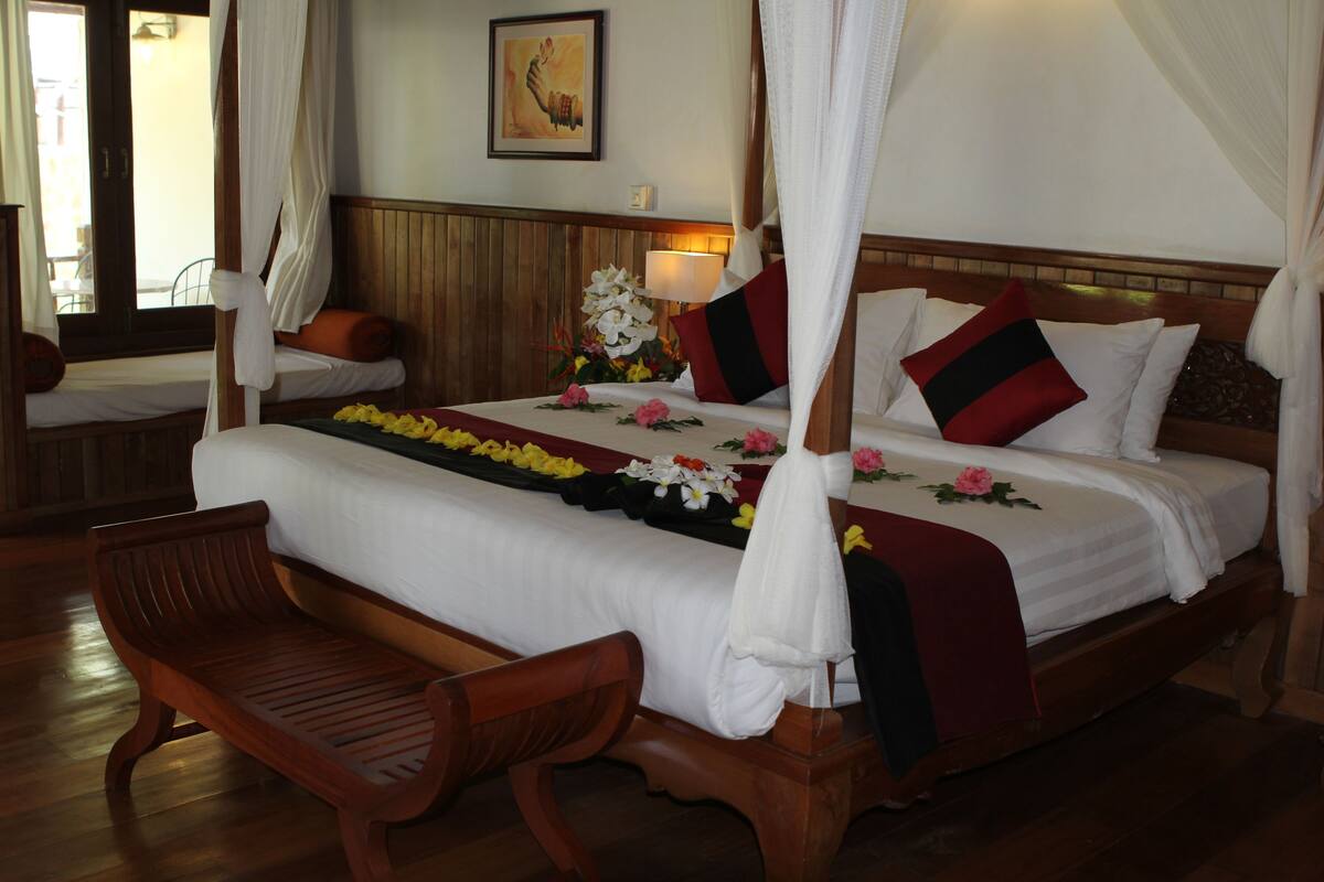 A four-poster bed with a canopy, a wooden bench, and a floral arrangement on the bed.