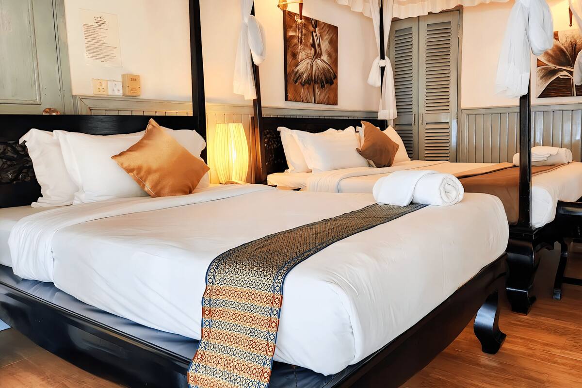 A hotel room with two beds, a wooden floor, a black bench, and a wall-mounted artwork.