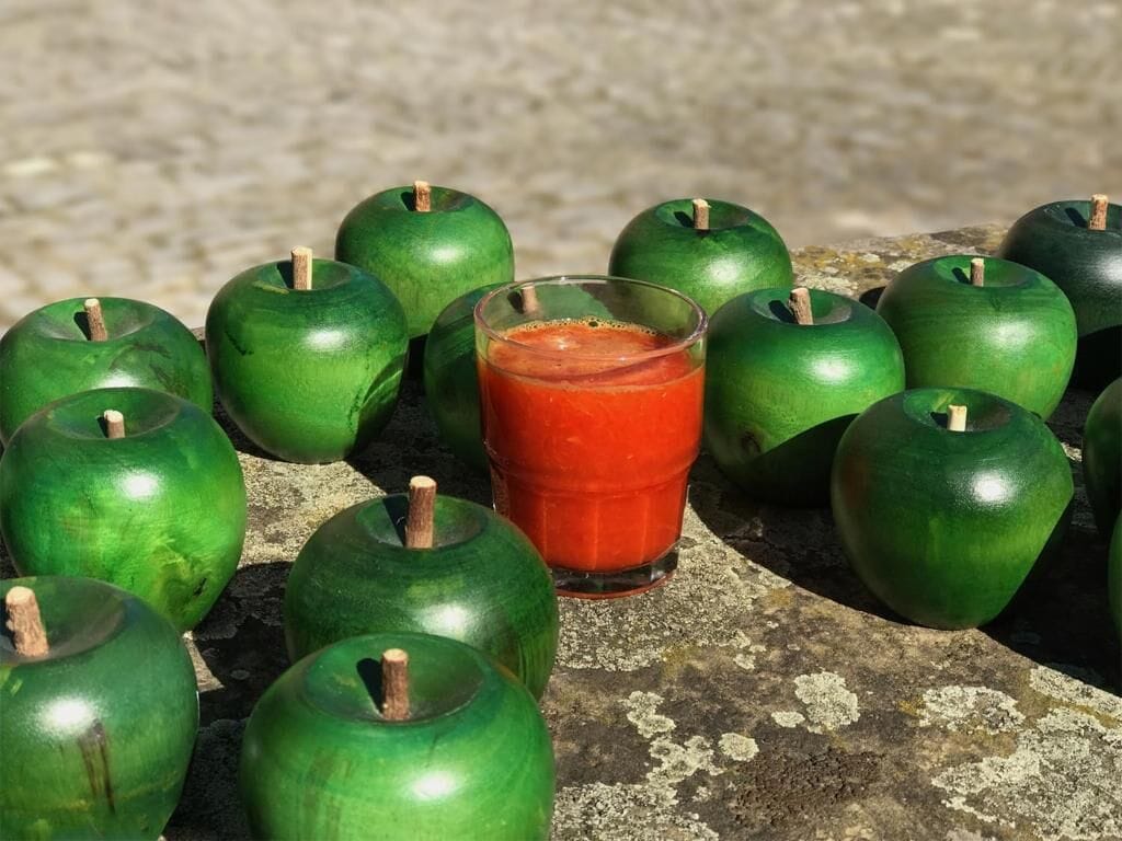 A collection of green apples and a glass of red juice on a stone surface.
