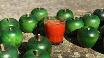 A collection of green apples and a glass of red juice on a stone surface.