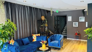 A modern living room with a blue sofa, a matching armchair, and a round coffee table. There is a staircase in the background leading to another level. - DORMERO Schwäbisch Hall (Schwäbisch Hall)