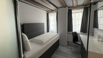 A modern hotel room with a bed, a desk, and a chair.