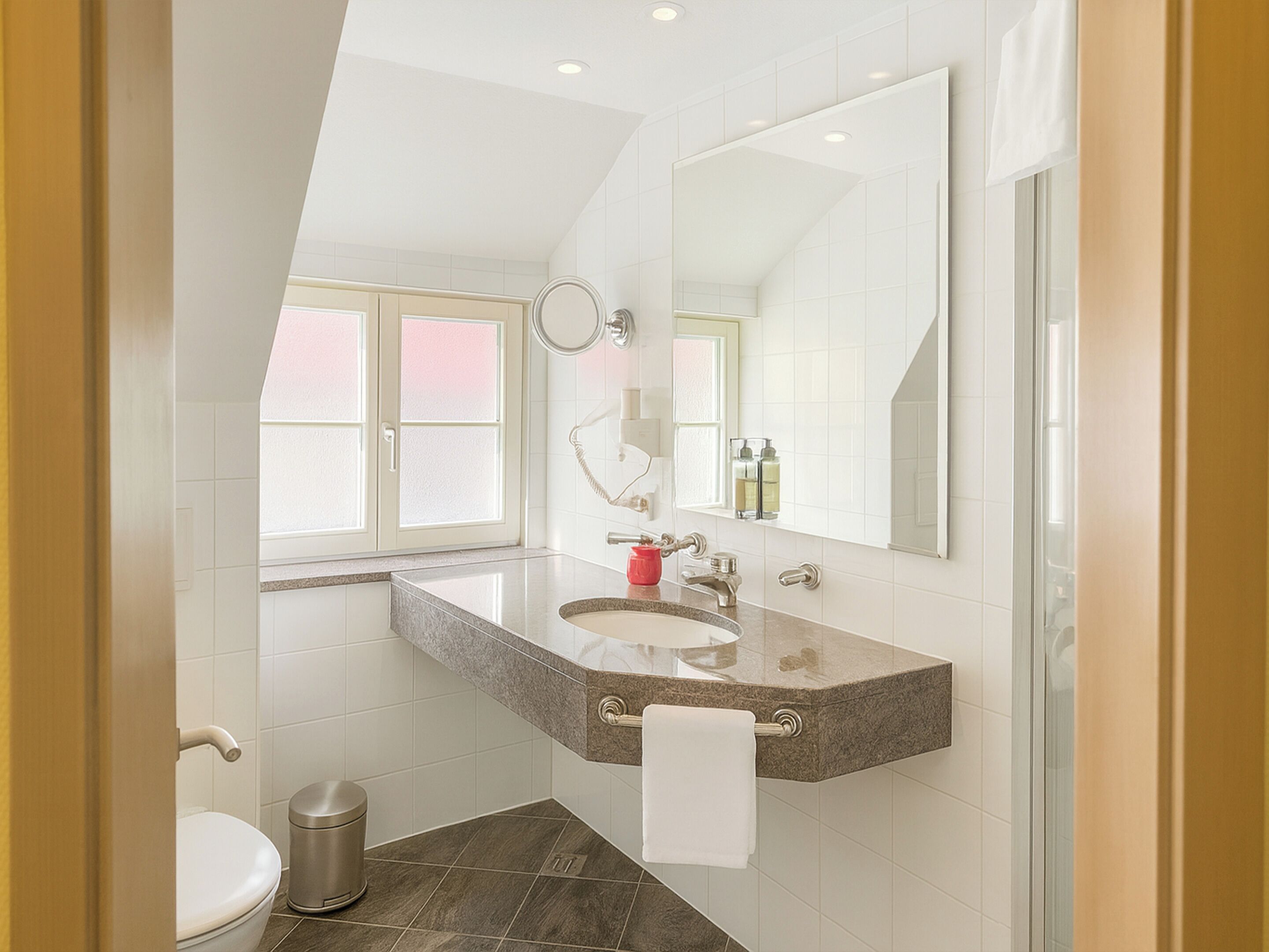 Een moderne badkamer met een marmeren wastafel, een grote spiegel en een toilet.