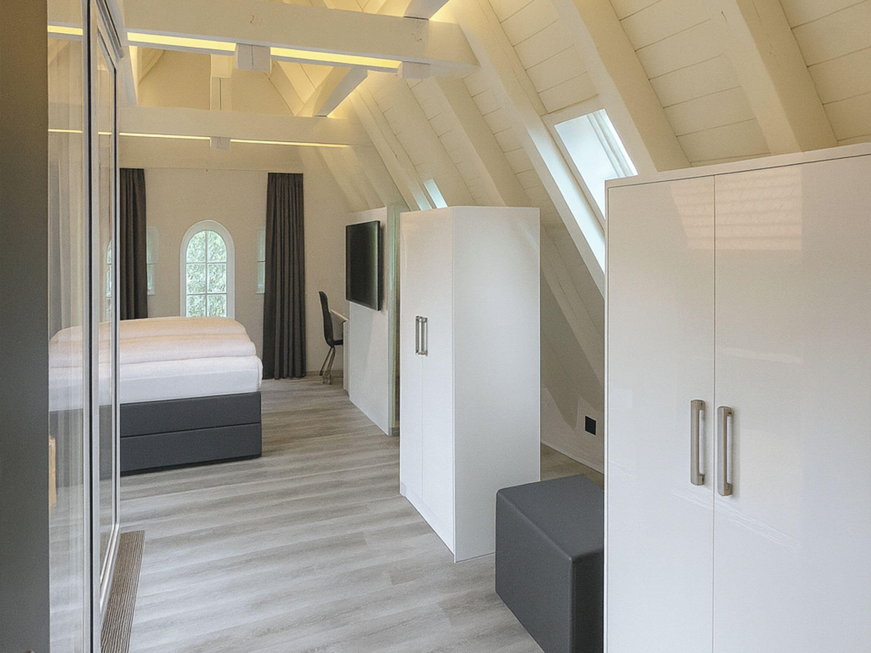 A modern bedroom with a sloped ceiling, a large bed, a wardrobe, and a television.