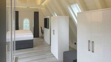 A modern bedroom with a sloped ceiling, a large bed, a wardrobe, and a television.