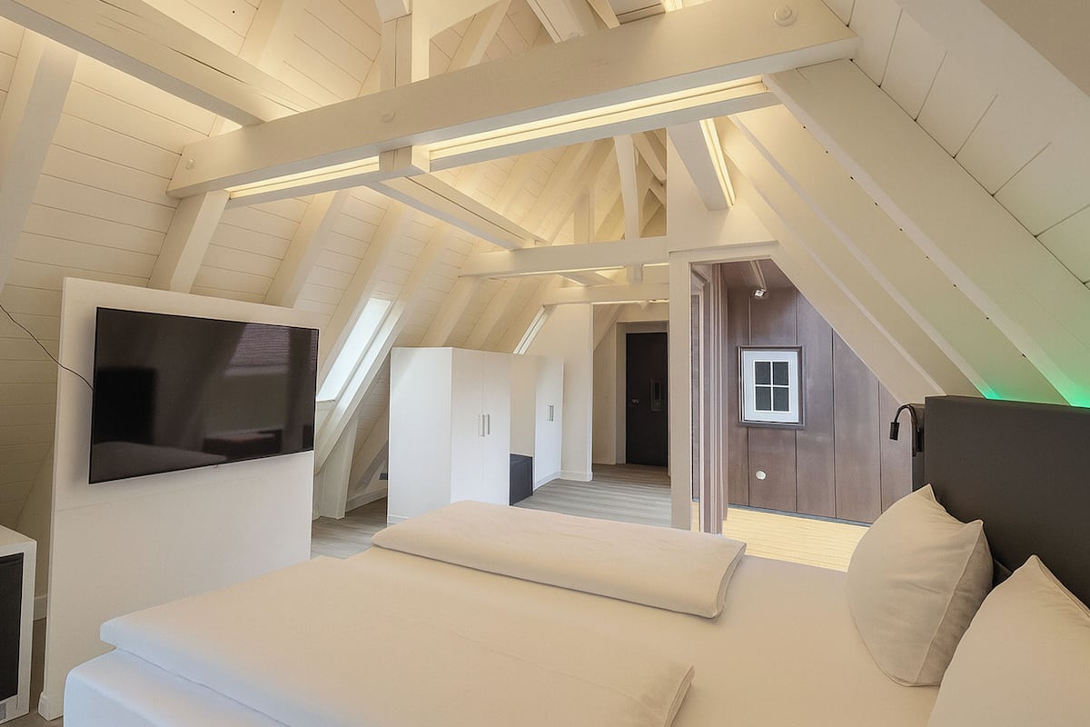 Een moderne loft slaapkamer met een schuine kap, een flatscreen televisie aan de muur, een groot bed met kussens en een inloopkast.