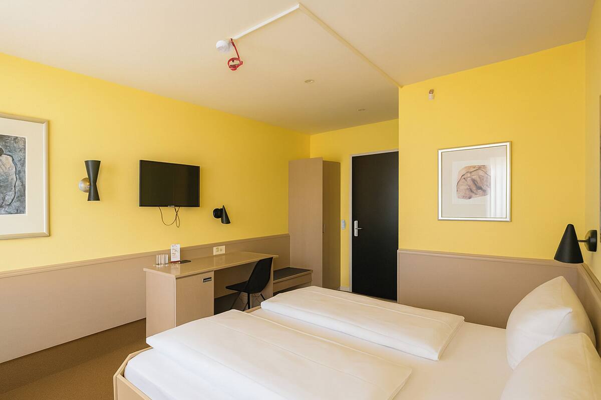 Een hotelkamer met een bed, bureau, stoel, televisie, kledingkast en kunstwerken aan de wanden.