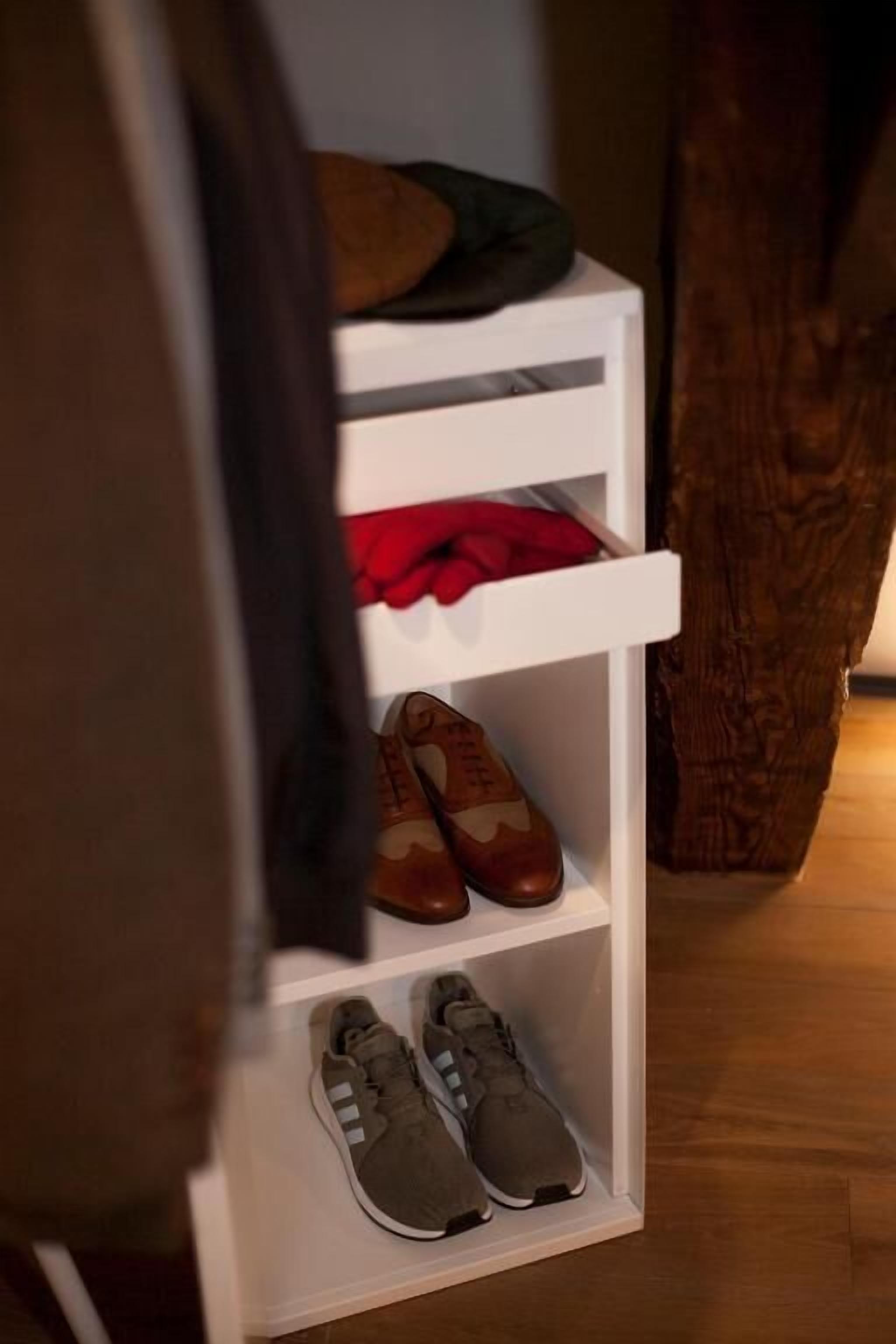 A white shoe rack with three shelves, each holding different pairs of shoes.