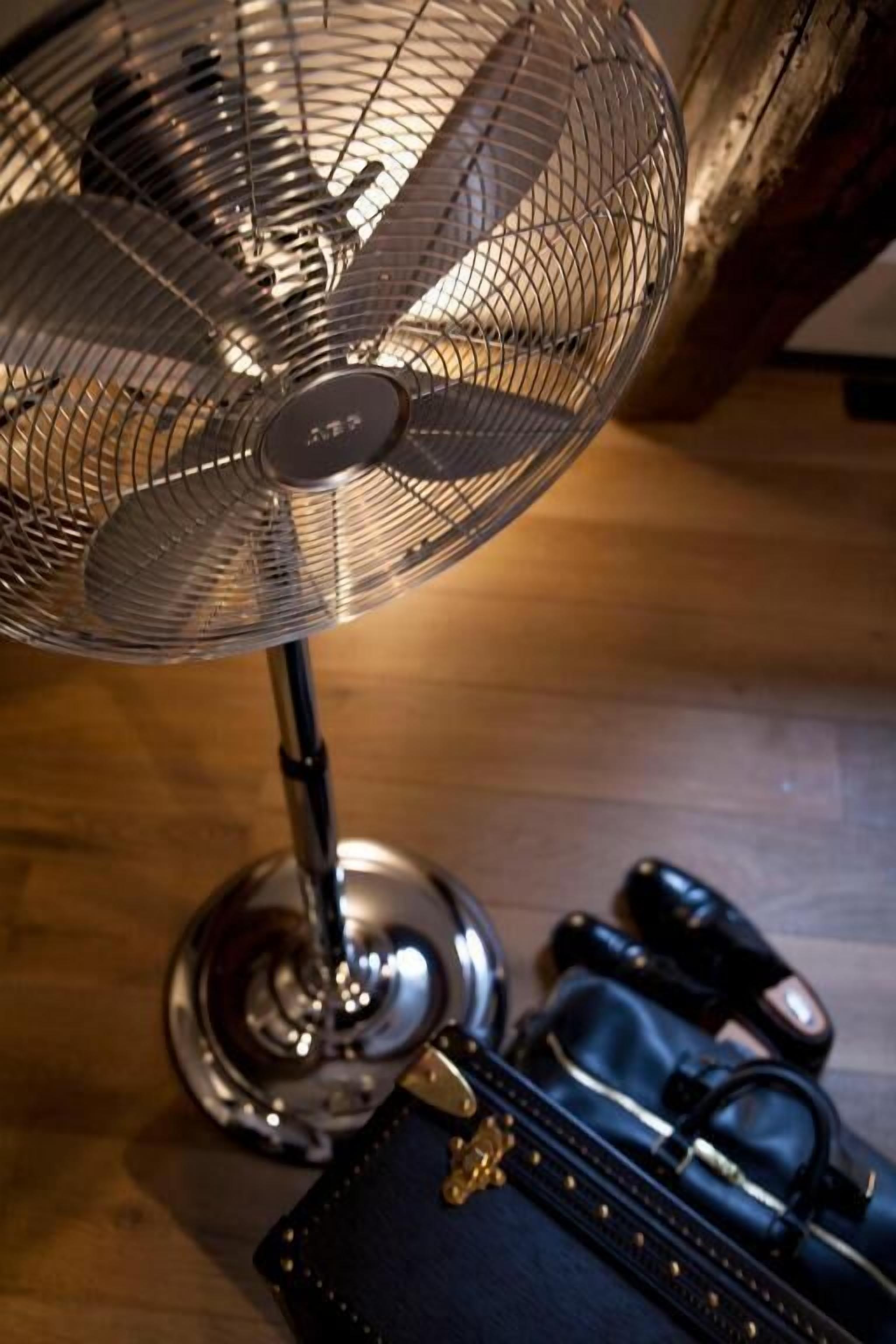 Een staande ventilator met een metalen voetstuk en een beschermkap op een houten oppervlak.