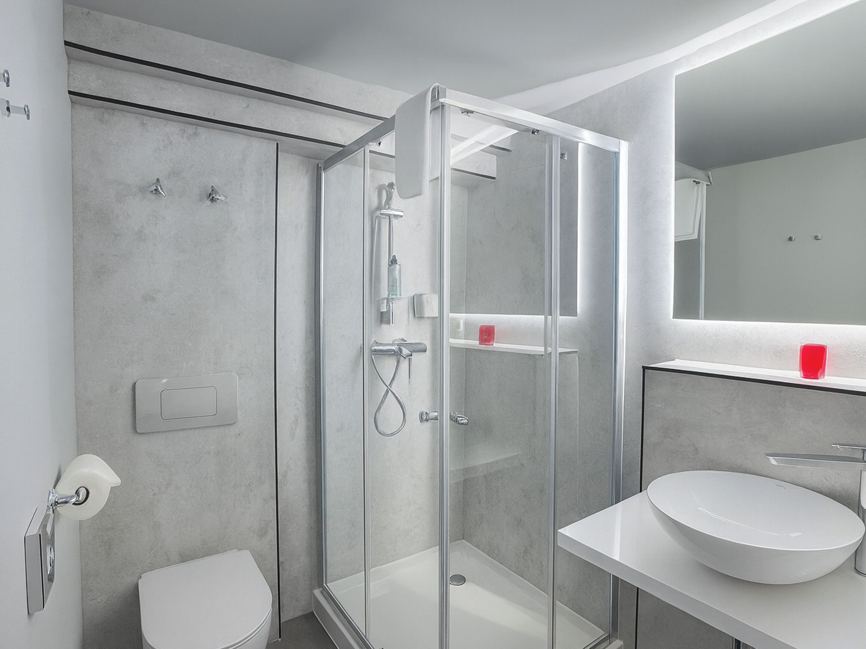 Un baño moderno con ducha envuelta en cristal, un lavabo blanco y un espejo sobre él.