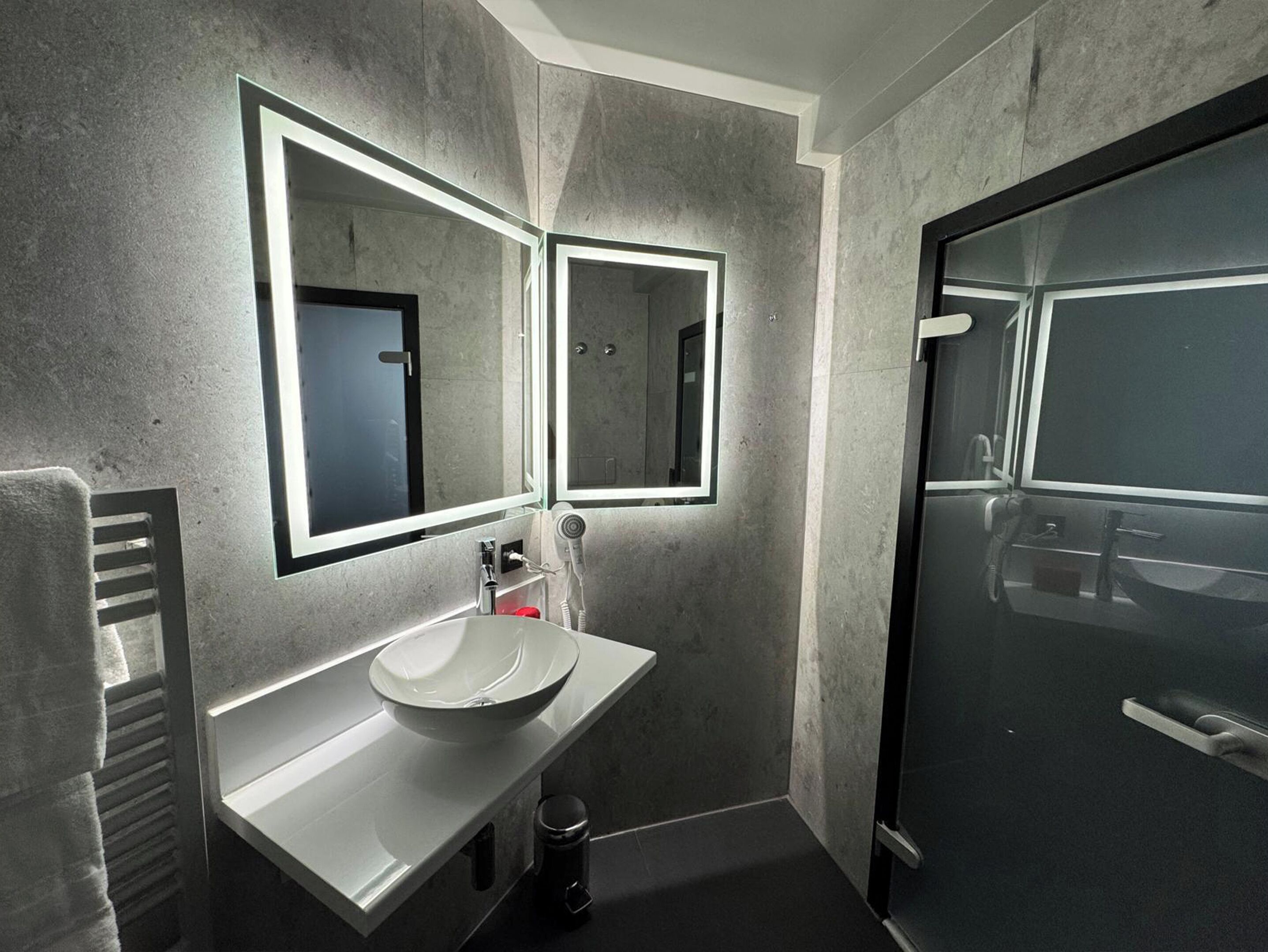 Un baño moderno con un espejo grande, un lavabo y una zona de ducha.