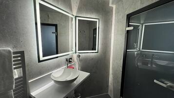 Un baño moderno con un espejo grande, un lavabo y una zona de ducha.