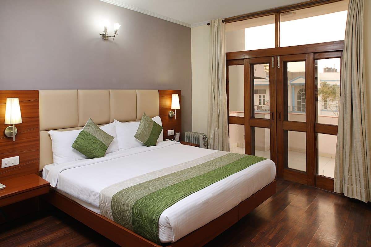 Habitación de hotel con una cama grande, cabecera de madera, dos lámparas de noche, vista a través de una puerta de vidrio y un radiador.