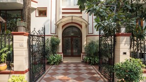 A checkered tile entrance to a building with a central doorway, flanked by potted plants and a wrought iron gate. - Ahuja Residency, Dlf Phase II (Gurugram)