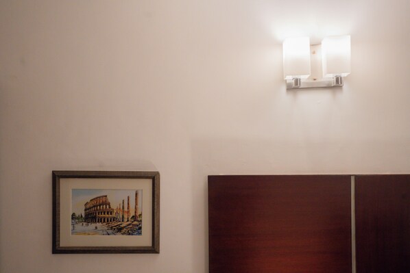 Un cuadro enmarco de un edificio histórico, un aplique de pared y un cabecero de madera.