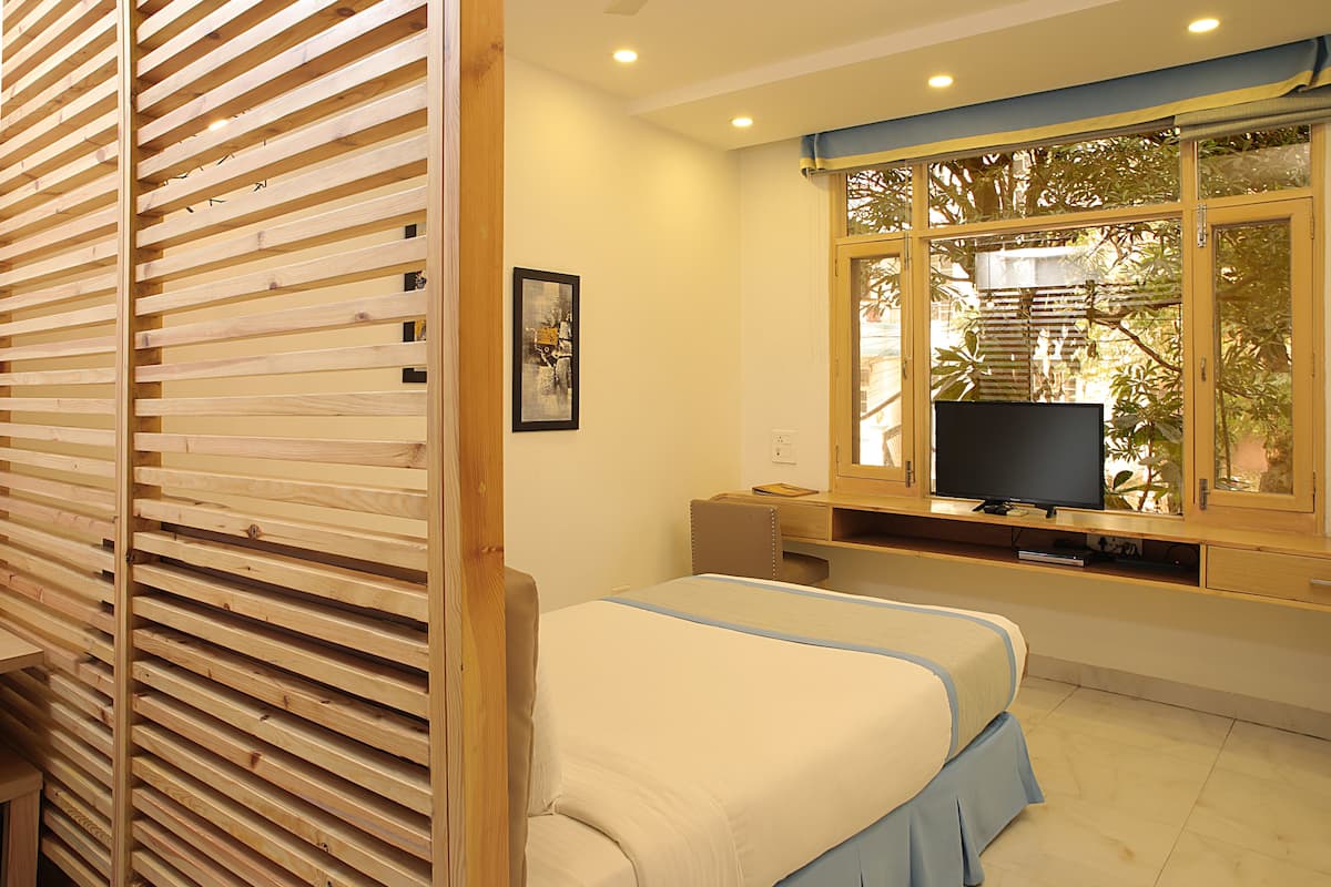 Un dormitorio con cama, televisión sobre un mueble, ventana con vista a árboles y separador de madera.