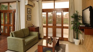 A living room with a green sofa, a glass coffee table, a potted plant, a television, and a sliding glass door leading to a balcony. - Ahuja Residency, Dlf Phase II (Gurugram)