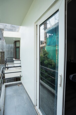 A narrow corridor with a glass door leading to a balcony. A staircase is visible on the left, and a green netting is seen through the door. - Ahuja Residency, Dlf Phase II (Gurugram)