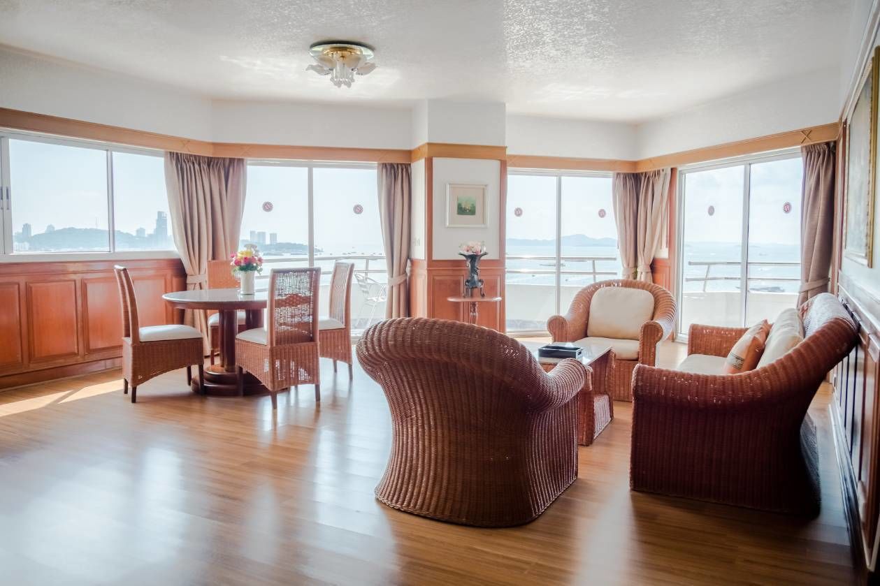 A spacious room with a wooden floor, a round dining table with chairs, a sofa, and a large window offering a view of the city skyline.