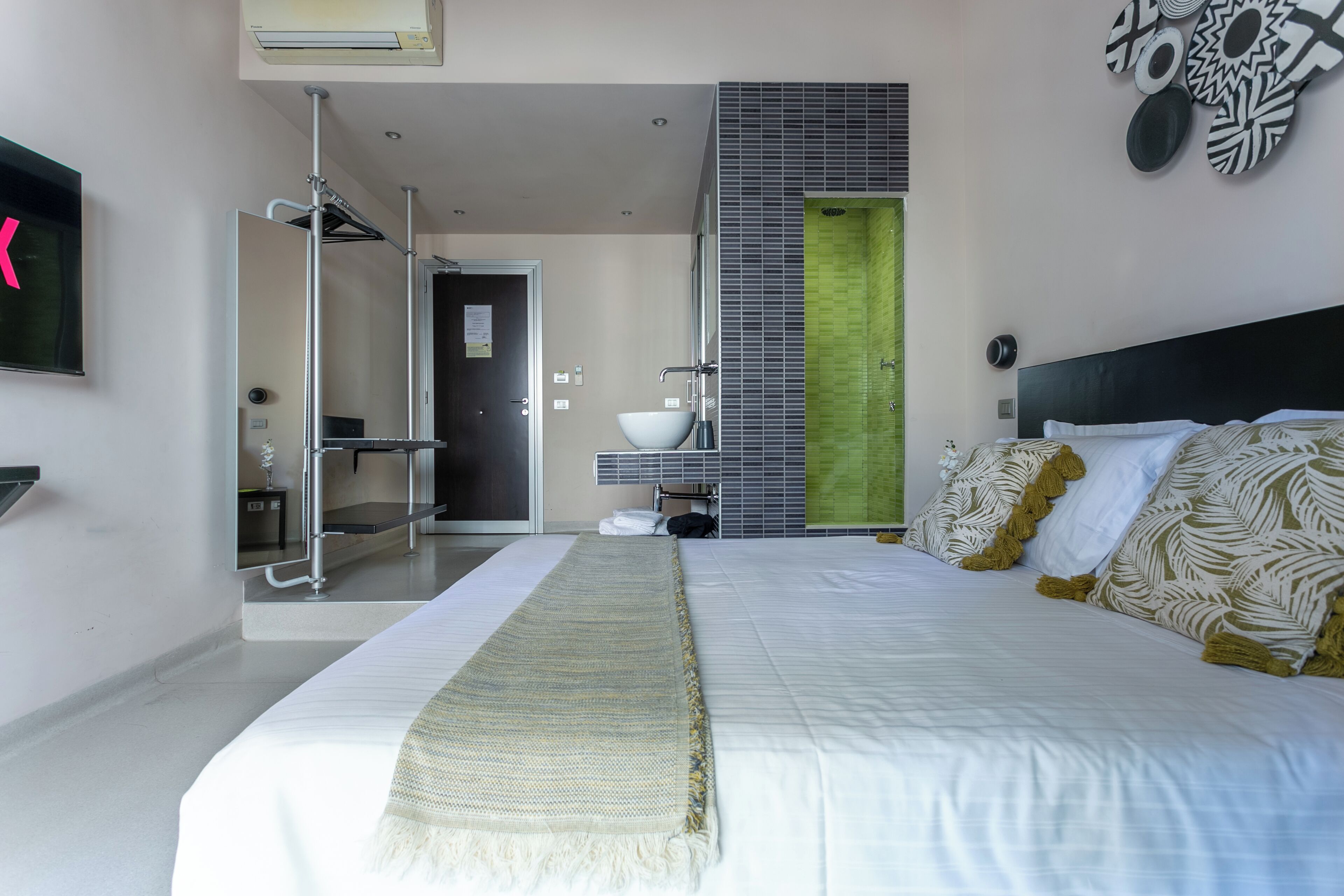 Una camera d'albergo moderna con un grande letto, un armadio a tutta parete, un bagno con doccia e una parete verde decorativa.
