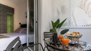 Una camera da letto moderna con un letto, una porta scorrevole in vetro che si apre su un balcone e un angolo colazione sul balcone.