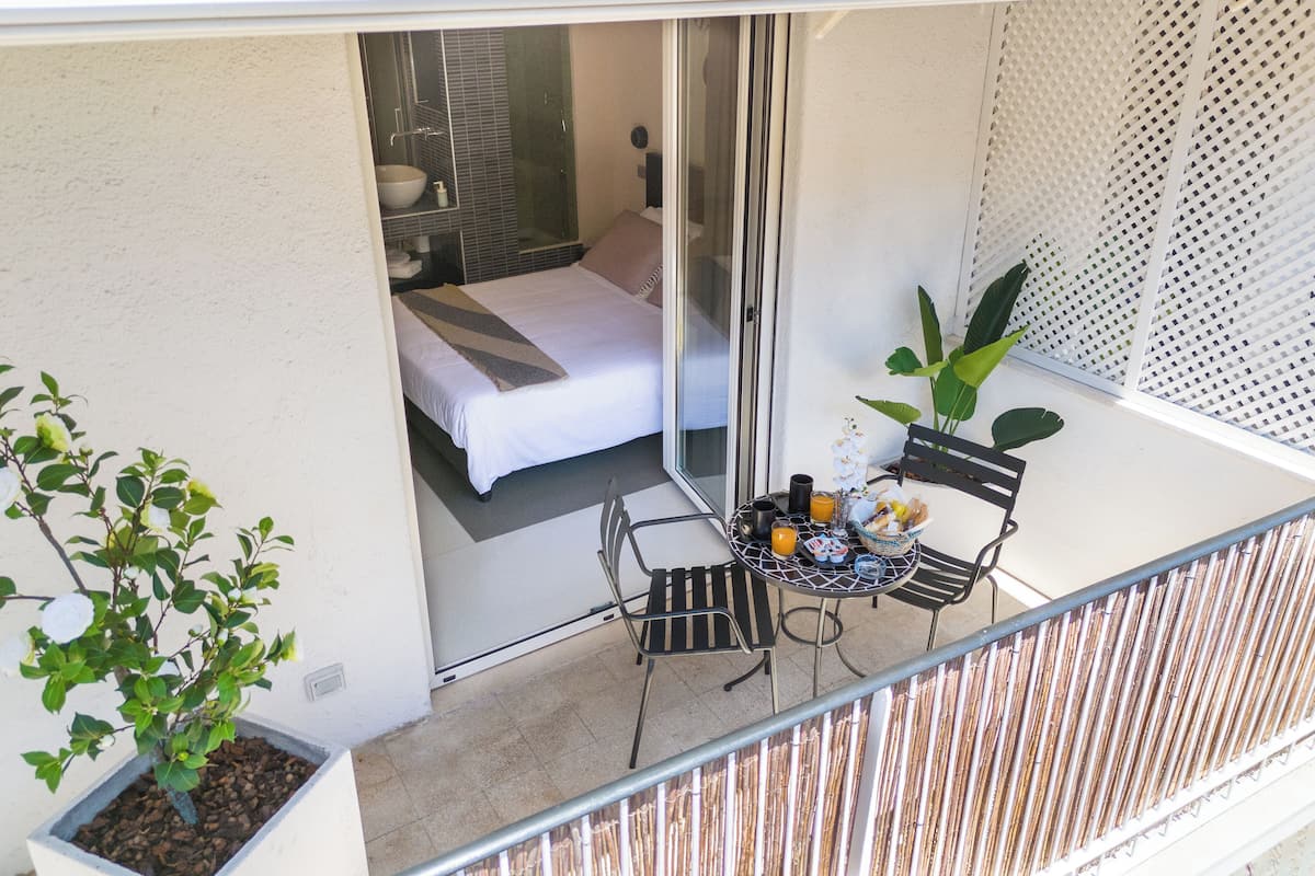 A balcony with a bed, a small table with drinks, and a potted plant.