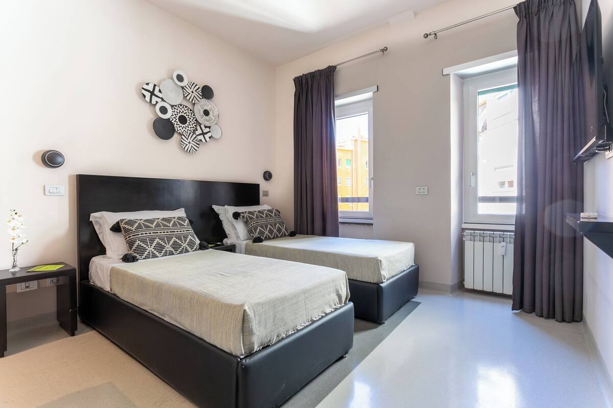 A modern bedroom with two beds, a wall art piece, a bedside table, and a view of the outside.