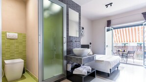 Camera d'albergo moderna con cabina doccia in vetro, un letto grande, bagno con WC e lavabo, e balcone con mobili da esterno.