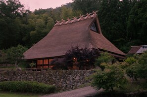A traditional Japanese house with a sloped roof, wooden beams, and a stone wall foundation.