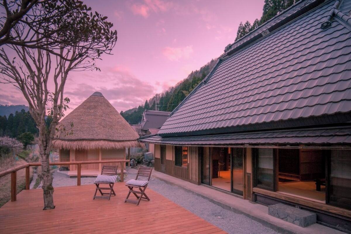 A wooden deck with two chairs, a thatched-roof structure, and a modern building with large windows.
