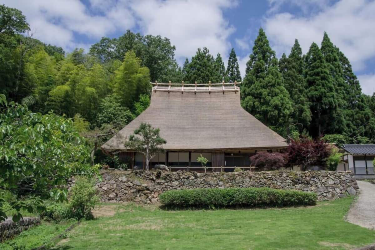 A traditional Japanese building with a sloped roof, surrounded by lush greenery and stone walls.