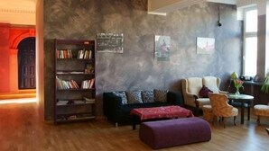 A living room with a dark-colored sofa, a bookshelf, a coffee table, and a purple ottoman. - El hostel (Warsaw)