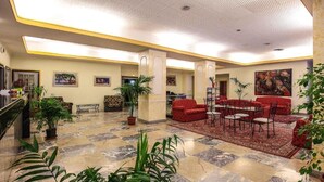 Un hall amplio con suelo de mármol, zona de estar con asientos rojos y plantas en macetas.