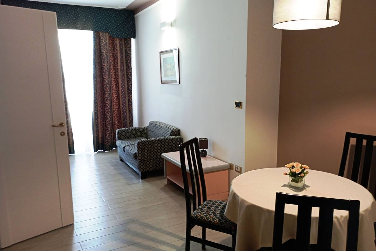 A room with a dining table, chairs, a sofa, and a lamp.