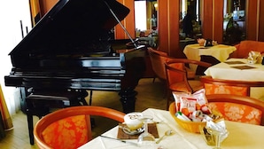 Un comedor con un piano de cola, mesas con manteles blancos y sillas.