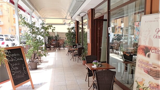 Un café al aire libre con mesas y sillas, plantas en macetas y un menú en la pizarra.