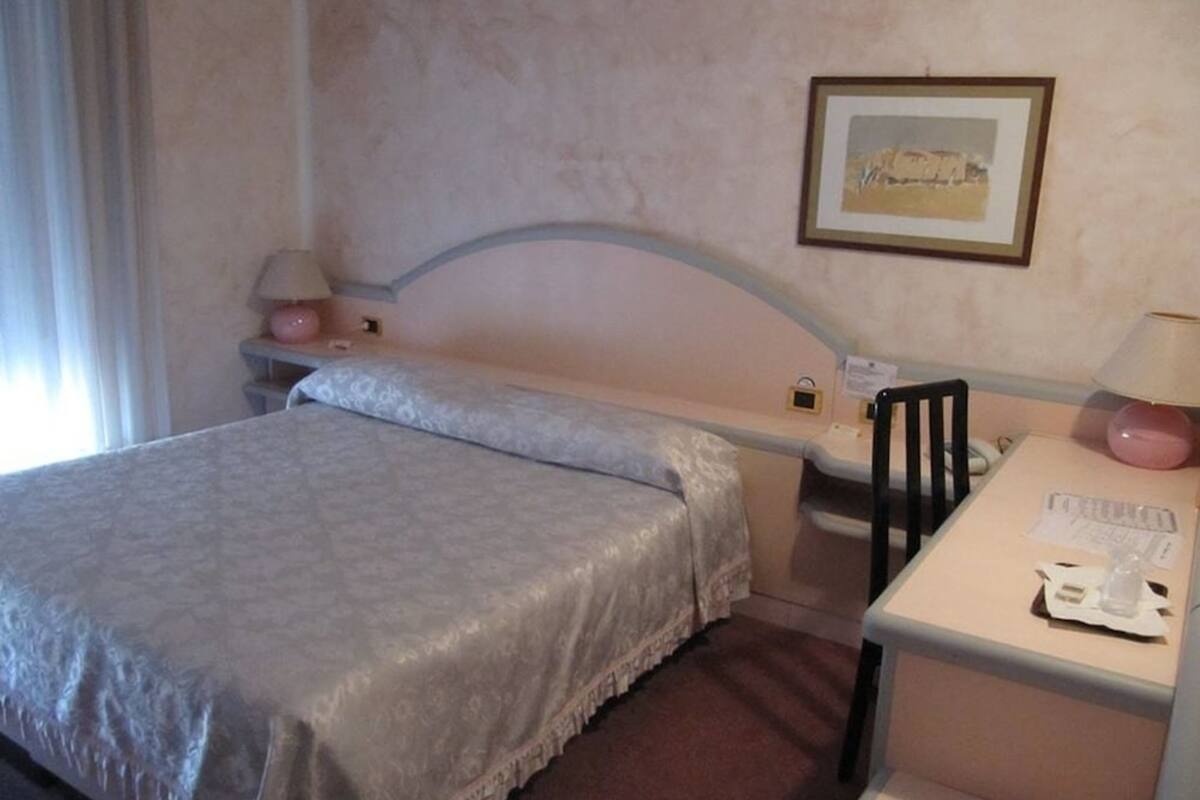 A hotel room with a single bed, a desk with a chair, a lamp, and a framed picture on the wall.