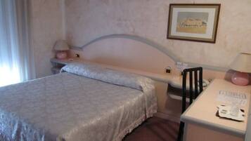 Una habitación de hotel con una cama individual, un escritorio con silla, una lámpara y un cuadro en la pared.